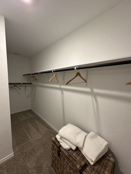 A spacious walk-in closet with ample hanging space, carpeted flooring, and a wicker basket for storage.