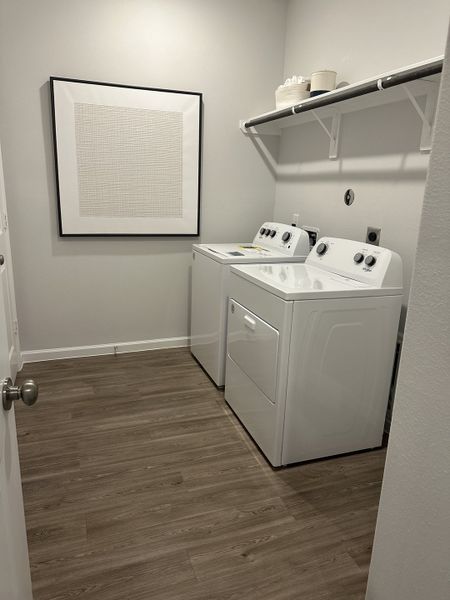A functional laundry room with modern appliances, wood-style flooring, and minimalist artwork. A functional laundry room with modern appliances, wood-style flooring, and minimalist artwork.