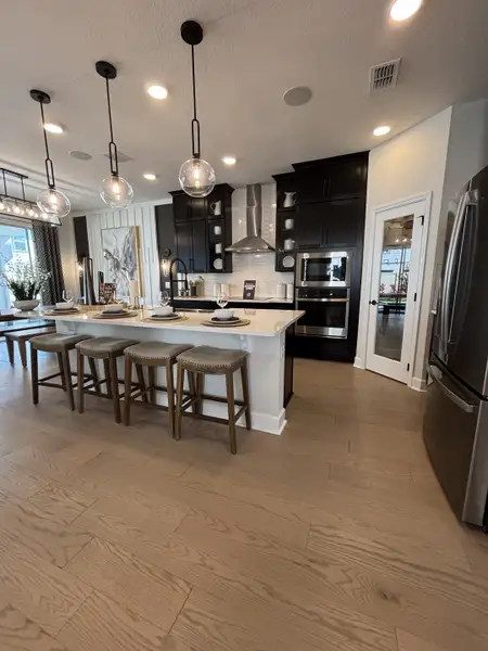 A sleek, modern kitchen with white cabinetry, stainless steel appliances, and pendant lighting in Eden at Crossprairie by M/I Homes (St. Cloud, FL).