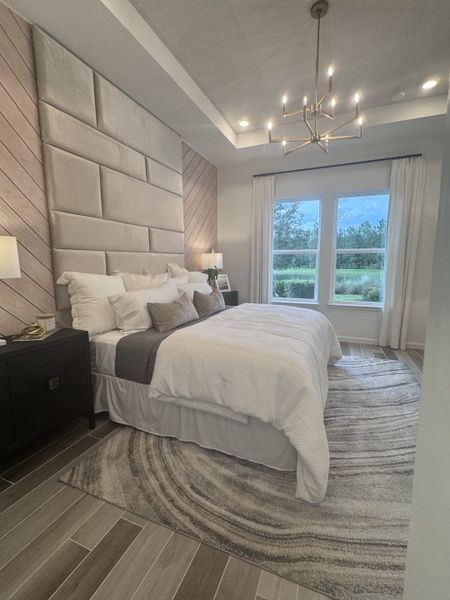 A luxurious bedroom with a plush accent wall, modern chandelier, and large window offering serene views.