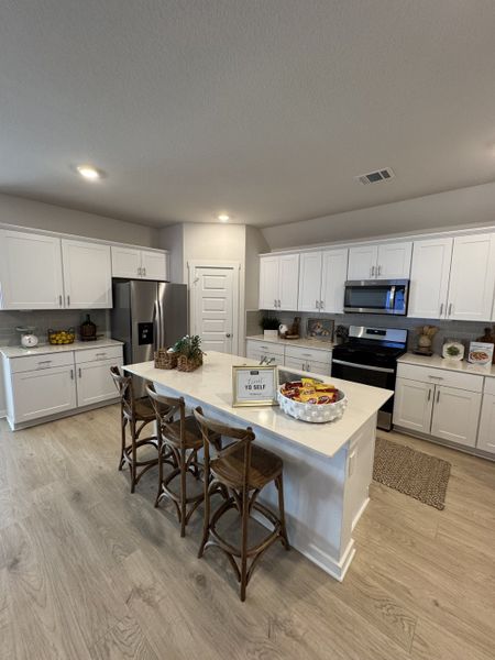 A spacious kitchen with sleek white cabinets, a large island, and rustic bar stools, perfect for entertaining and family gatherings.