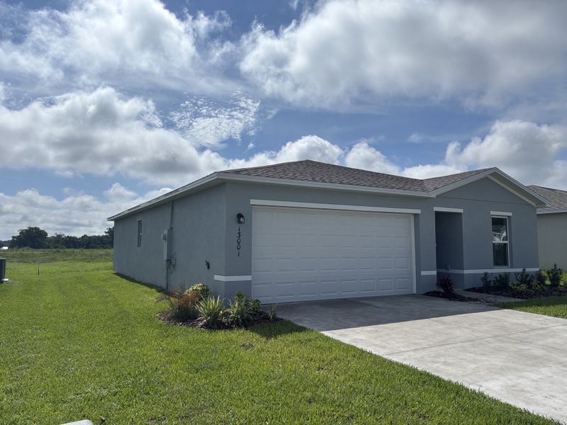 A charming gray home with a spacious driveway and lush lawn in Bennah Oaks by Century Complete (Belleview, FL).