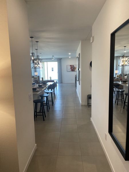 A sleek hallway with tiled flooring leads to bright open spaces, featuring contemporary pendant lighting and chic decor.