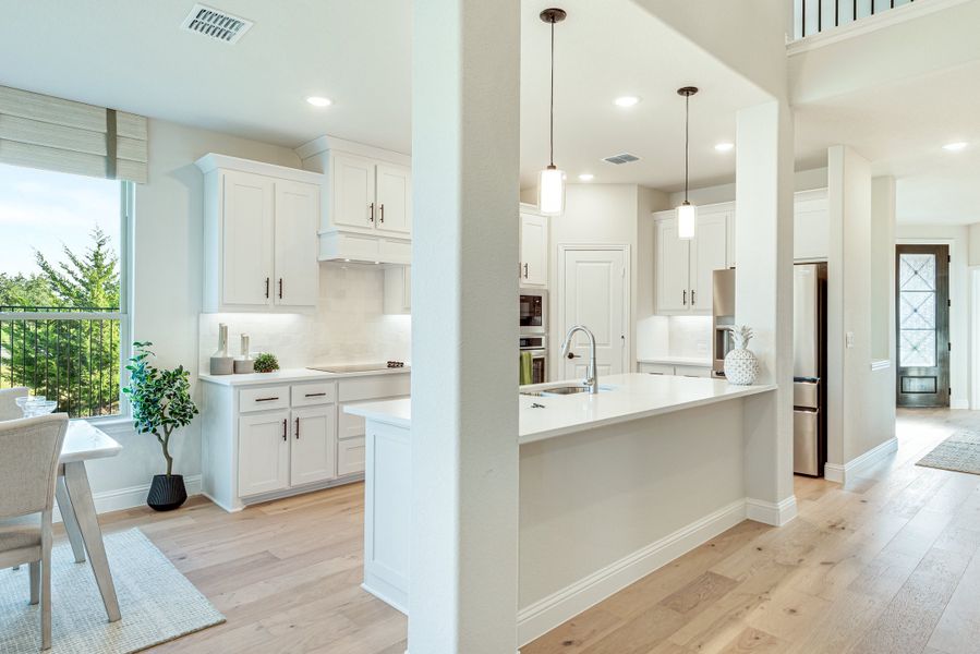 Open kitchen with white cabinets, island with sink, pendant lights, and light hardwood floors Open kitchen with white cabinets, island with sink, pendant lights, and light hardwood floors