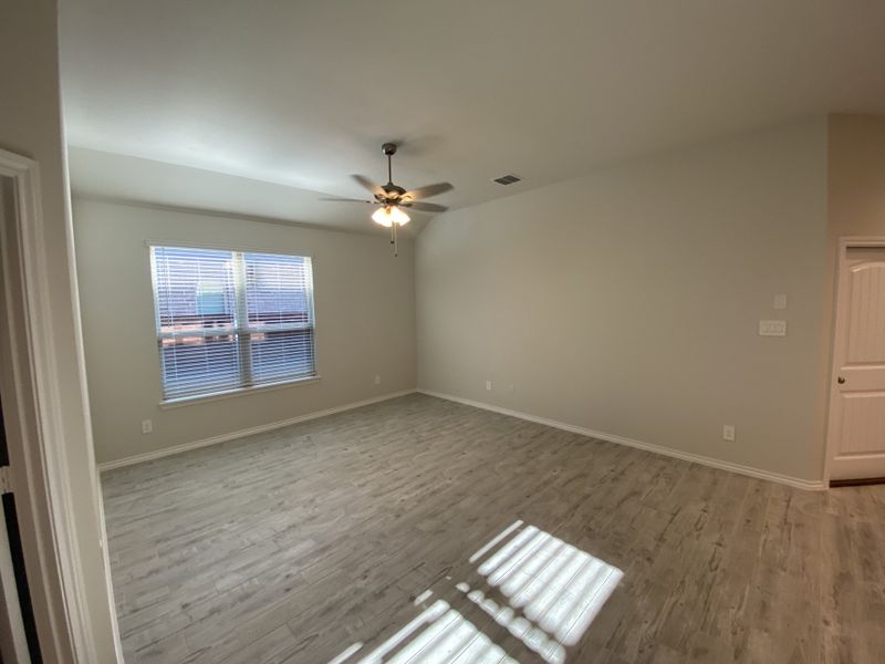 An open, bright room featuring elegant wood flooring, a ceiling fan, and ample natural light through a large window.
