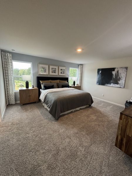 A cozy bedroom with plush carpeting, a stylish bed, dual windows, and modern decor accents.