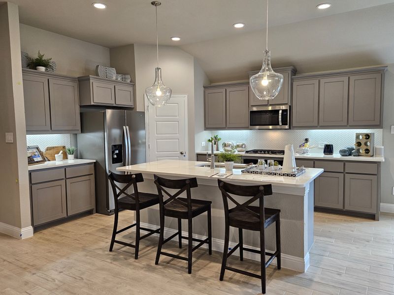 A modern kitchen featuring gray cabinets, a sleek island with stools, and elegant pendant lighting. A modern kitchen featuring gray cabinets, a sleek island with stools, and elegant pendant lighting.