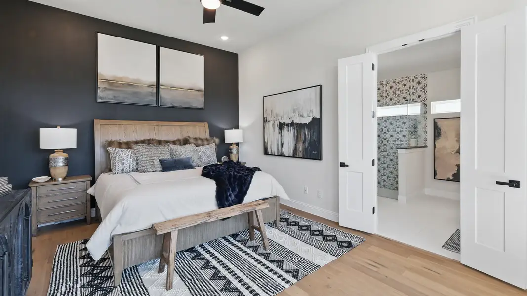 Elegant primary bedroom with a bold accent wall, wood flooring, and direct access to the en-suite bath. Elegant primary bedroom with a bold accent wall, wood flooring, and direct access to the en-suite bath.
