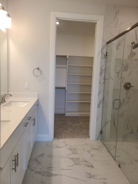 Luxurious bathroom featuring marble-like flooring, sleek glass shower, and spacious vanity leading to a walk-in closet. Luxurious bathroom featuring marble-like flooring, sleek glass shower, and spacious vanity leading to a walk-in closet.