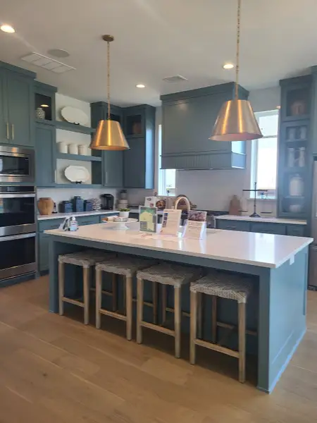 A modern kitchen with blue cabinetry, gold pendant lights, and a large island with woven stools.