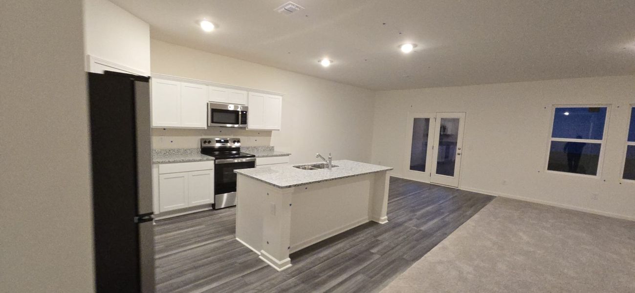 Modern kitchen with granite countertops, white cabinets, and stainless steel appliances, adjacent to a spacious living area.