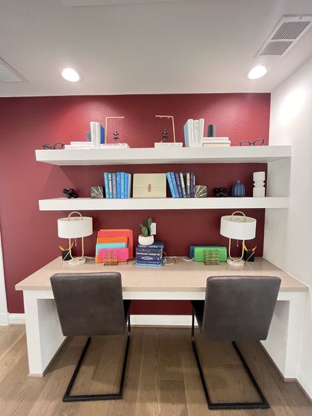 A chic home office with a red accent wall, floating shelves, dual desks, and modern decor.