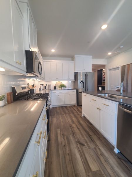 A spacious kitchen with sleek countertops, white cabinetry, stainless steel appliances, and wood flooring.