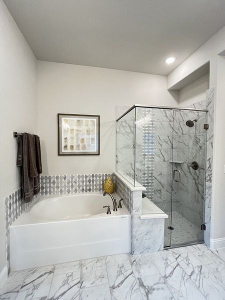 A luxurious bathroom featuring a marble-tiled bathtub, glass shower, and elegant patterned accents.