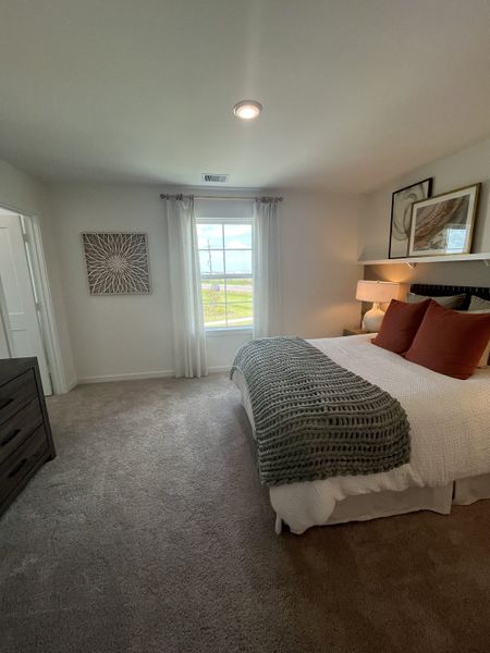 A cozy bedroom featuring neutral decor, a large window, and a plush bed with throw pillows and a knitted blanket.