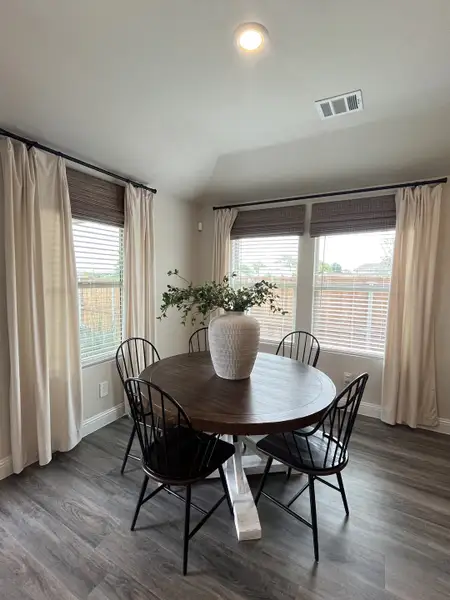A cozy dining area with a round wooden table, elegant chairs, and large windows adorned with soft drapes. A cozy dining area with a round wooden table, elegant chairs, and large windows adorned with soft drapes.