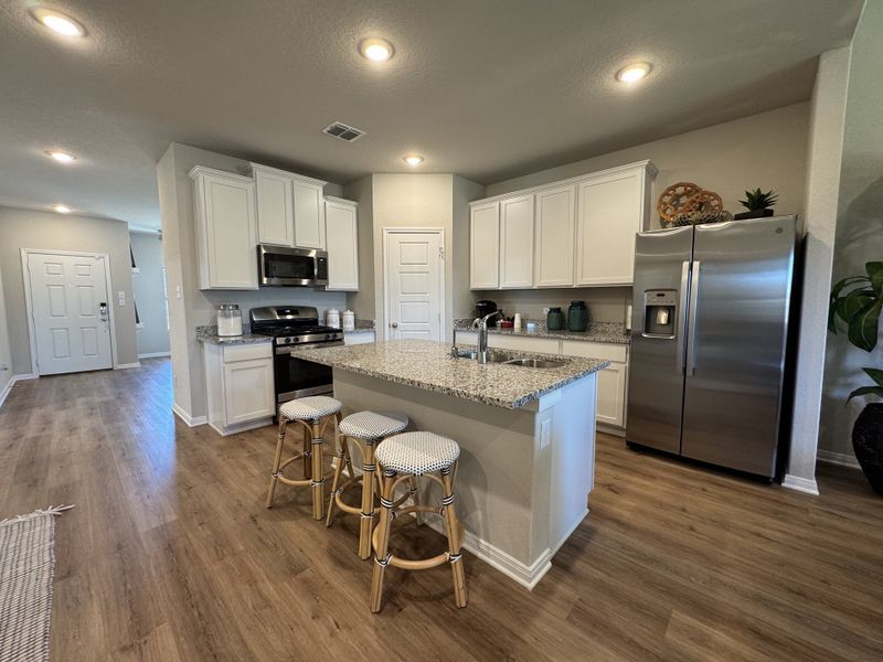 A modern kitchen with granite countertops, white cabinets, and stainless steel appliances.