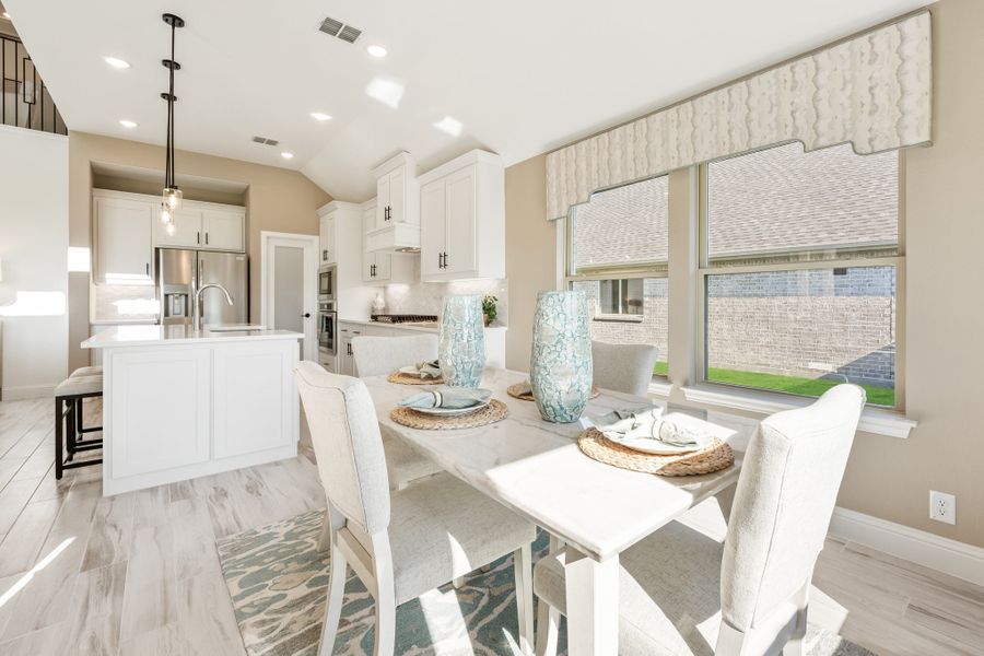 Dining area with white table and chairs open to kitchen with white cabinets and stainless steel appliances