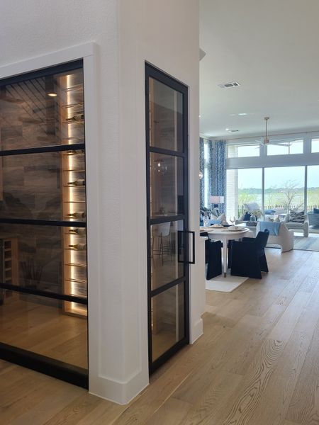 A modern, open-concept living area with sleek glass wine storage, light wood floors, and abundant natural light. A modern, open-concept living area with sleek glass wine storage, light wood floors, and abundant natural light.