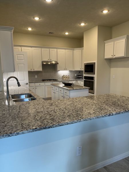 A modern kitchen featuring granite countertops, white cabinetry, and stainless steel appliances, illuminated by recessed lighting.