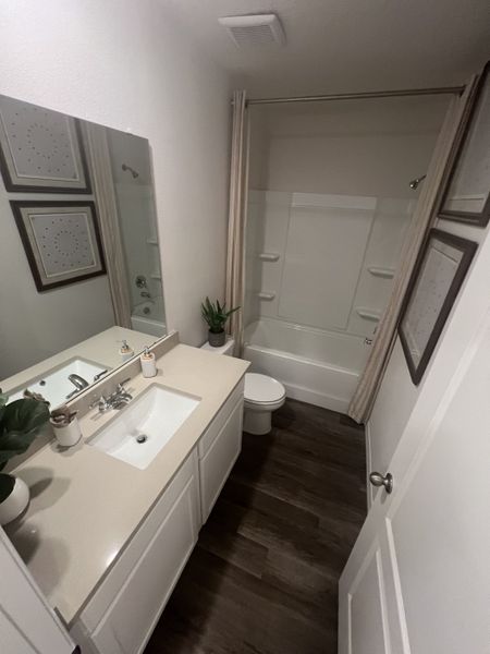 A modern bathroom with sleek white cabinetry, a spacious tub, dark wood flooring, and minimalist decor.