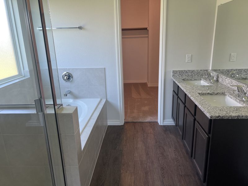 A modern bathroom featuring a tiled bathtub, double granite vanity, and a large mirror.