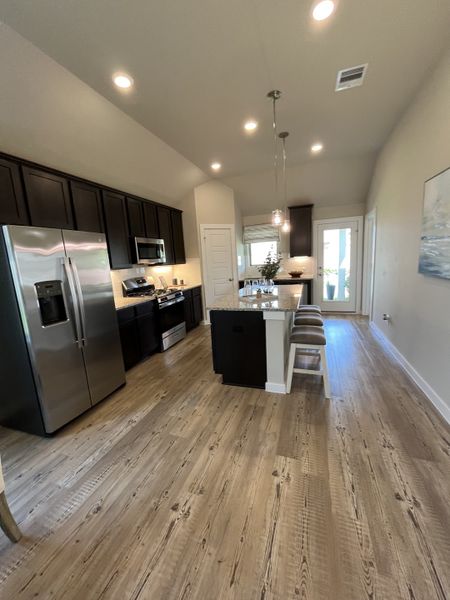 A modern kitchen featuring sleek dark cabinets, a spacious island, and elegant lighting on polished wood floors.