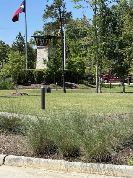 Lush green community entrance with flagpoles in River's Edge by Legend Homes (Conroe, TX).