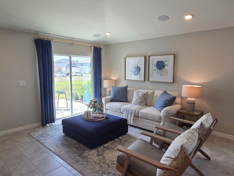 A cozy living room with a plush white sofa, blue curtains, and stylish decor, offering a bright view to the outside patio.