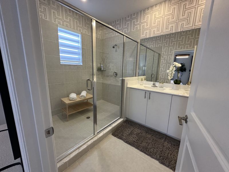 A sleek bathroom with a large glass shower, modern vanity, and geometric wallpaper accents.