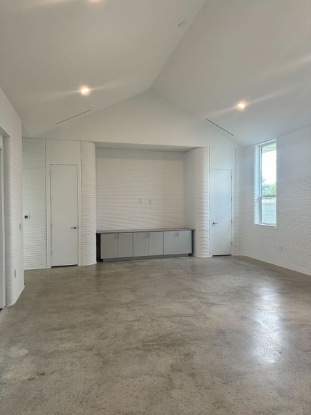 A spacious, minimalist room with a vaulted ceiling, polished concrete floor, and built-in cabinetry.