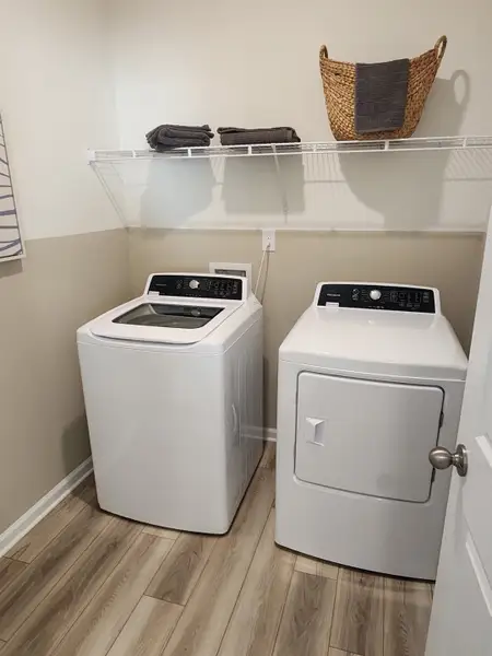 A spacious laundry room with wood-look flooring, overhead shelving, and modern appliances in Panther Creek by KB Home (Jacksonville, FL).