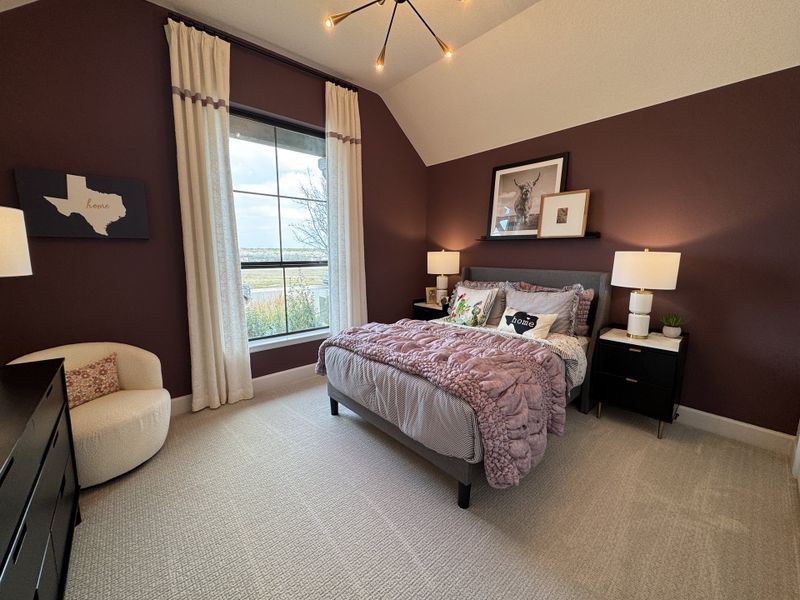 A cozy bedroom with burgundy accent wall, plush bedding, stylish lighting, and large window with scenic view.