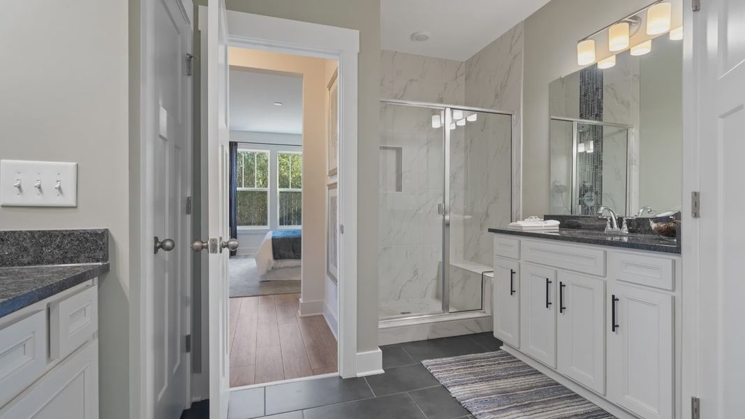 Primary suite with dark tile flooring, white tile shower, separate vanities with dark countertops and white cabinets Primary suite with dark tile flooring, white tile shower, separate vanities with dark countertops and white cabinets