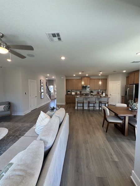 An open-concept living space featuring a cozy sofa, wood floors, and a modern kitchen with pendant lighting.