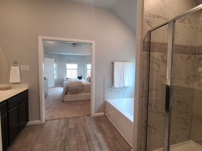 A modern bathroom featuring a marble-tiled shower, wood-look flooring, and a cozy view into a bright bedroom. A modern bathroom featuring a marble-tiled shower, wood-look flooring, and a cozy view into a bright bedroom.
