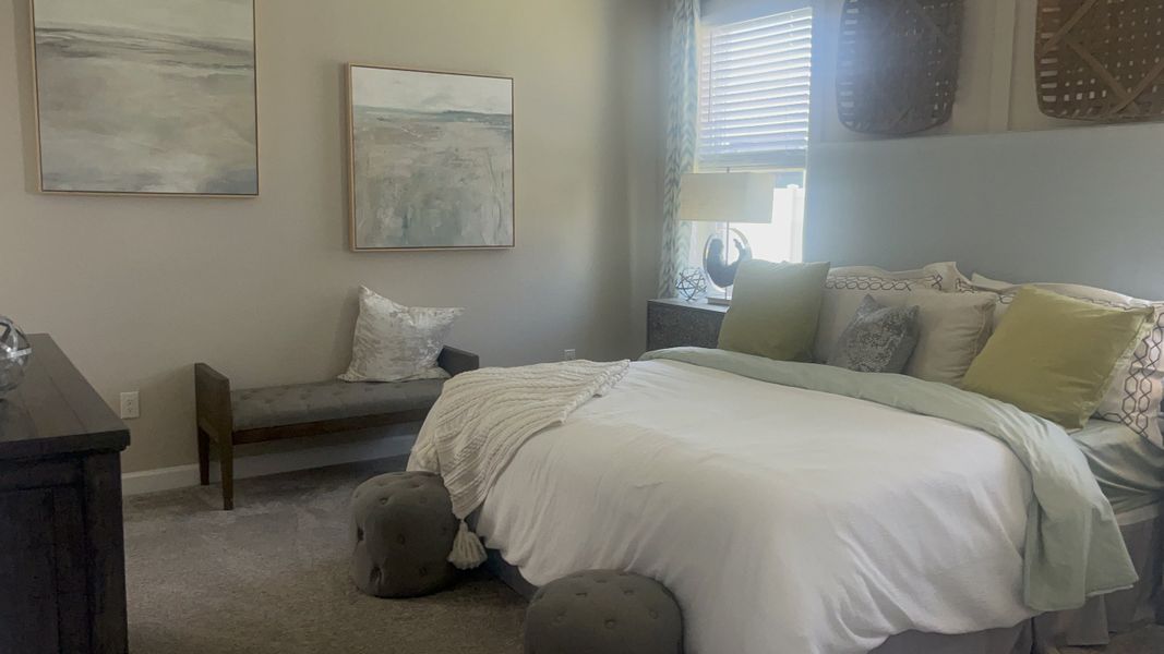 A cozy bedroom featuring a plush bed, subtle wall art, and a comfortable bench, bathed in natural light.