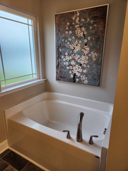 A cozy bathroom featuring a sleek tub, artistic floral painting, and frosted window for a serene atmosphere.