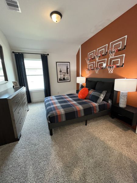 A cozy bedroom featuring a plaid bedspread, basketball-themed wall decor, and soft gray carpet flooring.
