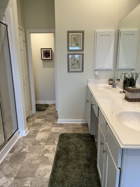 A bright bathroom with dual sinks, stylish art, tile flooring, and plush green rugs for a cozy feel.
