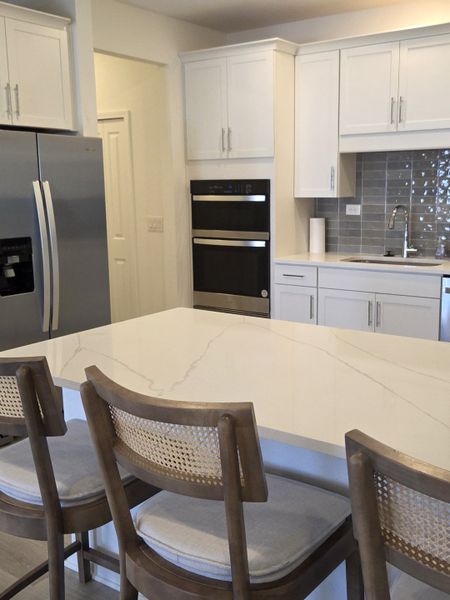 A modern kitchen with a sleek island, white cabinetry, stainless steel appliances, and stylish wooden barstools.