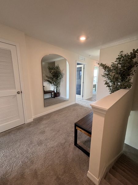 A bright upstairs landing with plush carpeting, a modern bench, and decorative accents in Avian Pointe Townhomes by D.R. Horton (Apopka, FL).