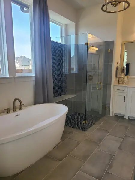 A modern bathroom featuring a sleek bathtub, glass shower, and elegant fixtures with ample natural light.