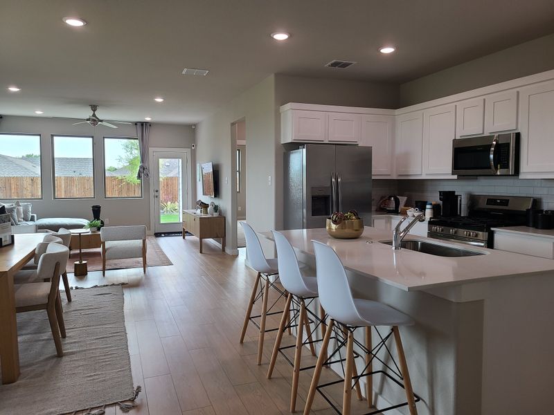 An open-concept kitchen and living area with sleek white cabinets, modern appliances, and stylish bar seating.
