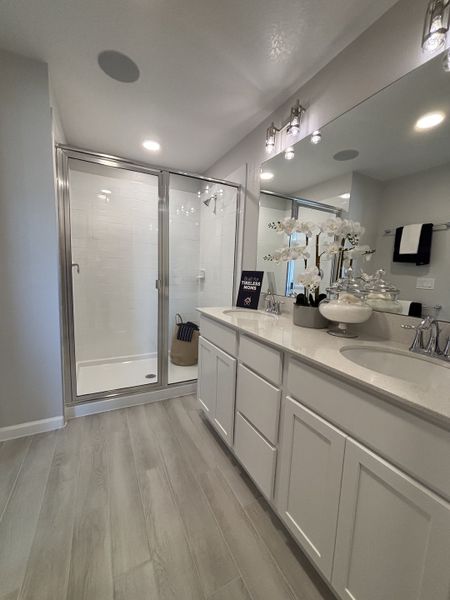 A stylish bathroom featuring a blue accent wall, a classic white vanity, and a tiled bathtub in Eden at Crossprairie by M/I Homes (St. Cloud, FL).