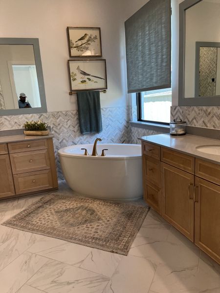 A cozy bathroom featuring a freestanding tub, elegant herringbone tile walls, and warm wood cabinetry.