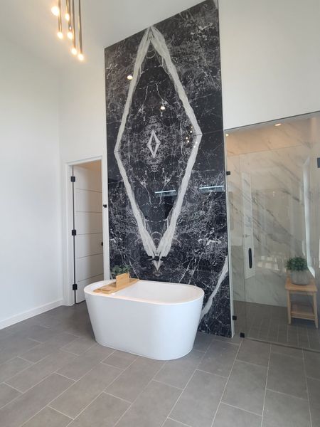A luxurious bathroom with a freestanding tub, striking black marble accent wall, and sleek tile flooring.