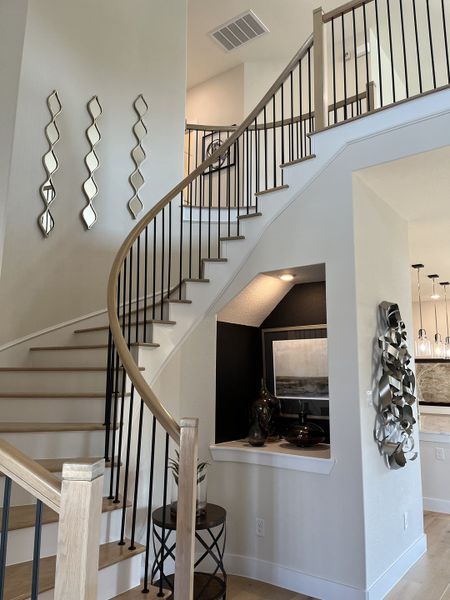 A modern staircase with sleek metal railings, decorative wall art, and elegant shelving in a contemporary hallway.
