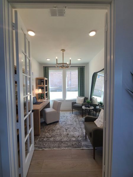 A cozy home office with elegant lighting, comfortable seating, a wooden desk, and large windows for ample natural light.