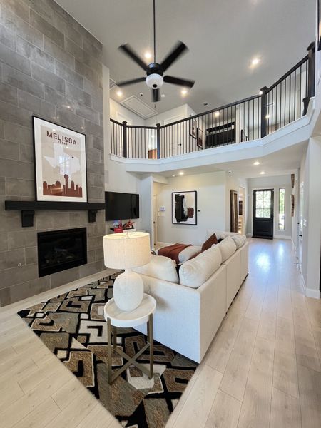 A spacious living room with a high ceiling, modern fan, cozy fireplace, and elegant decor.